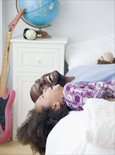 African father and daughter laughing on bed