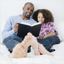 African father reading to daughter on bed