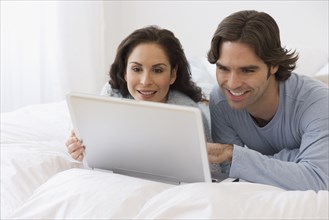 Hispanic couple using laptop on bed
