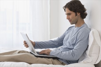 Hispanic man using laptop on bed