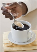African woman putting sugar in coffee