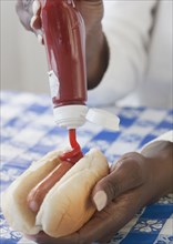 African woman putting ketchup on hot dog