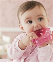 Mixed race baby girl chewing on plastic toy