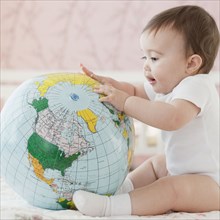 Mixed race baby girl looking at blow-up globe