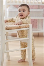 Mixed race baby girl balancing near chair