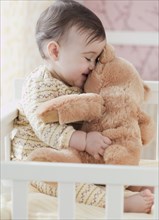 Mixed race baby girl snuggling teddy bear