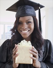 African woman in graduation cap and gown holding gift