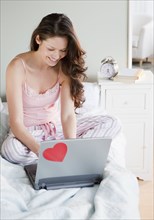 Mixed race woman using laptop on bed