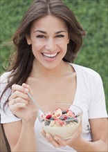 Hispanic woman eating cereal with fresh fruit