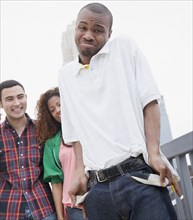 African man showing empty pockets with friends in background