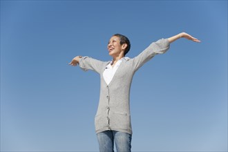 Chinese woman smiling with arms outstretched against blue sky