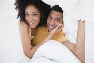 Smiling couple under bed sheet