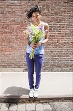 Mixed race woman holding bouquet on urban sidewalk
