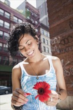 Mixed race woman picking petals off flower on urban street