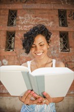 Mixed race woman reading book in front of urban building