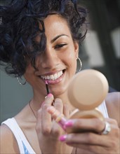 Mixed race woman applying lip gloss with compact mirror