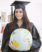 Mixed race graduate in cap and gown holding globe