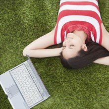 Mixed race woman sleeping in grass with laptop