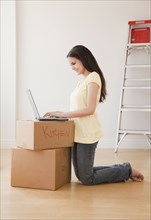 Mixed race woman using laptop on cardboard boxes