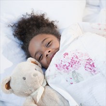 Mixed race girl in bed with teddy bear