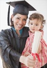 Hispanic mother graduate holding daughter and diploma