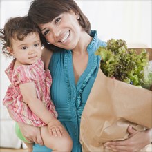 Hispanic woman carrying daughter and groceries