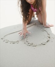 Hispanic girl drawing heart shape in sand