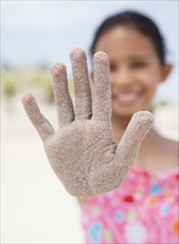 Hispanic girl displaying sand-covered hand