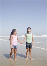 Hispanic sisters holding hands on beach