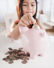 Mixed race girl putting coin in piggy bank