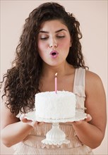 Mixed race woman blowing out candle on birthday cake