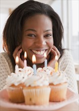 Mixed race woman with candle topped cupcakes