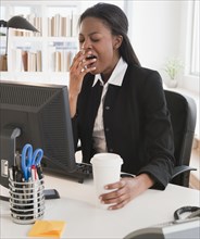 Mixed race businesswoman yawning at desk