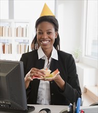 Mixed race businesswoman eating birthday cupcake