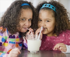 Hispanic sisters sharing glass of milk