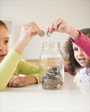 Hispanic sisters putting coins in jar
