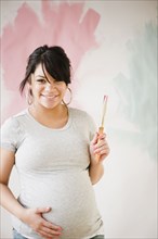 Pregnant Hispanic woman painting wall