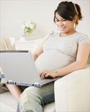 Pregnant Hispanic woman typing on laptop