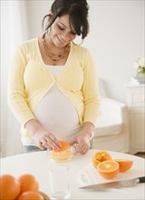 Pregnant Hispanic woman squeezing oranges