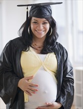 Pregnant Hispanic woman in graduation cap and gown