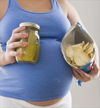 Pregnant Hispanic woman holding pickles and potato chips