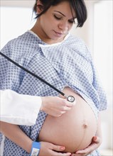 Pregnant Hispanic woman with doctor listening to stomach