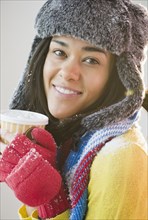 Mixed race woman in hat and gloves drinking coffee