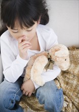 Chinese girl sucking thumb and holding teddy bear