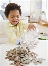 Black boy emptying jar of coins on table