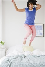Hispanic woman jumping on bed
