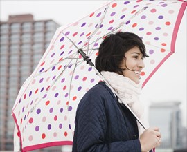 Hispanic woman walking in city with umbrella