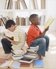 Boys sitting on stacks of books and reading
