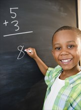 Black boy solving math problems on blackboard