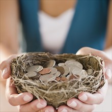 Mixed race woman holding nest filled with coins